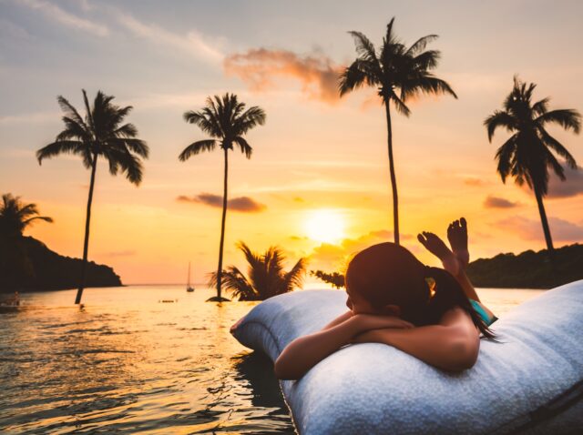 Summer vacation concept, Silhouette asian woman with bikini relax in infinity pool hotel resort with sea beach and palm tree background at sunset in Koh Kood, Thailand